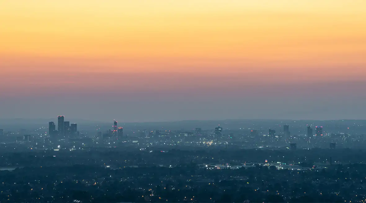 Panorama de Manchester au crépuscule avec des immeubles illuminés sous un ciel dégradé orange, rose bleu