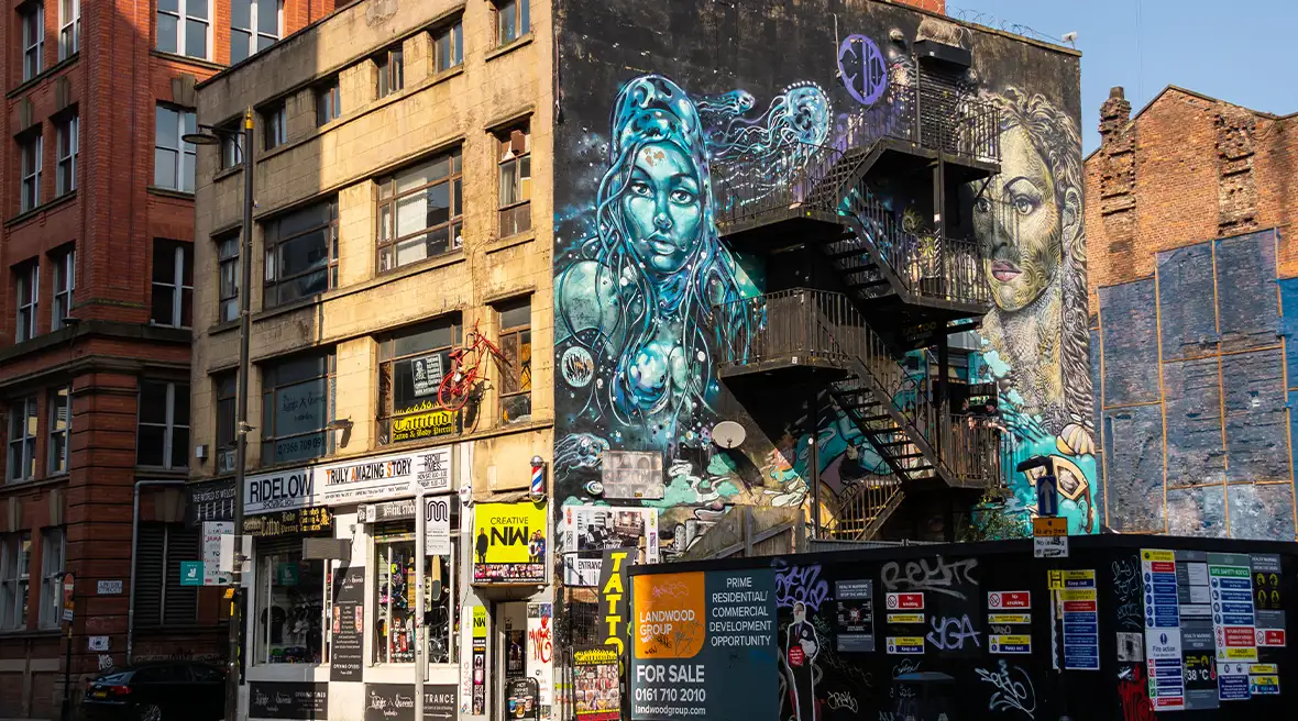 Escaliers de secours sur la façade d’un immeuble recouverte d’une fresque murale représentant des personnages dans les tons de bleu et noir au dessus d’une boutique