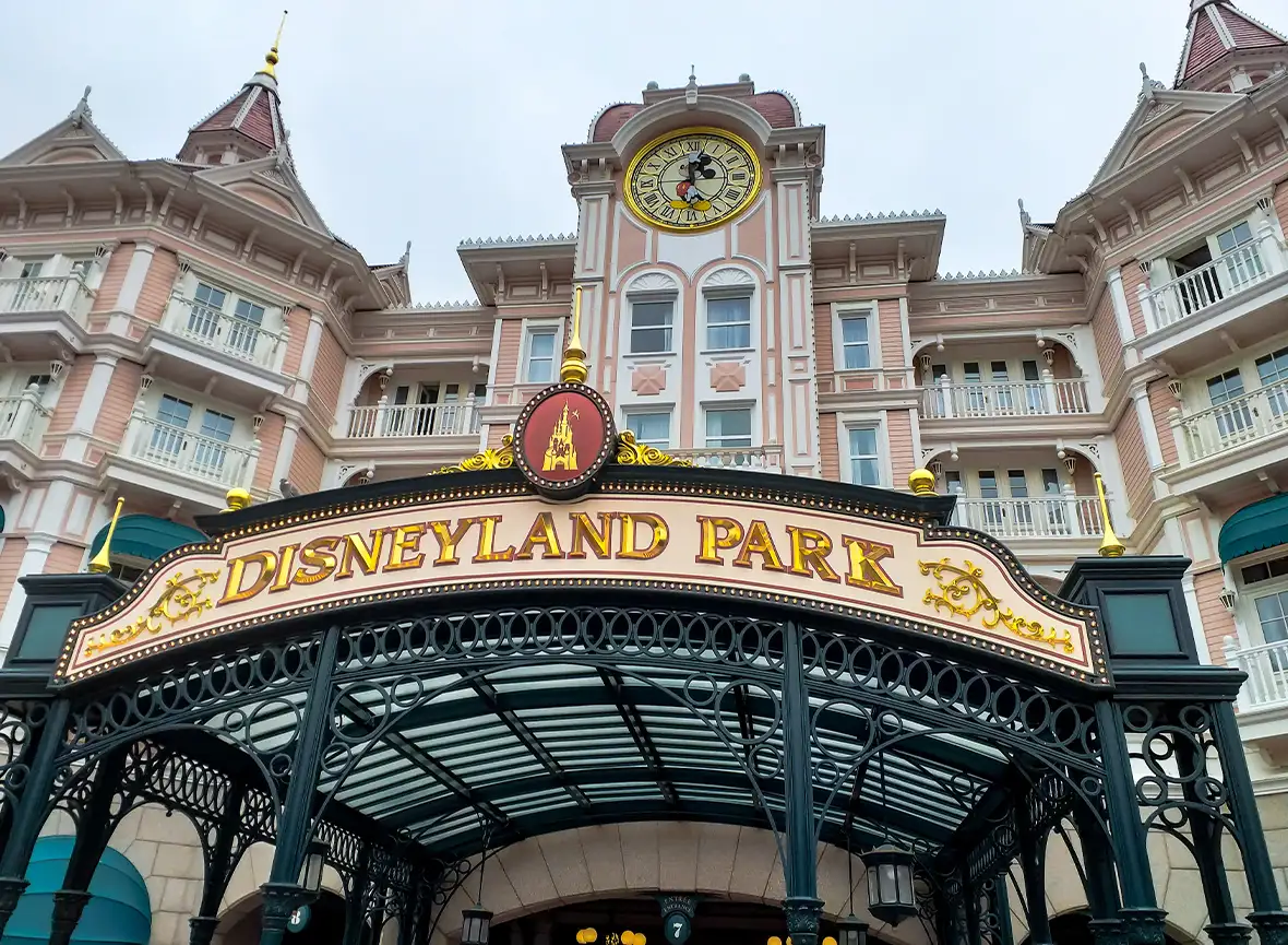 Pink and white doll house like building with mickey mouse clock and sign saying Disneyland Park