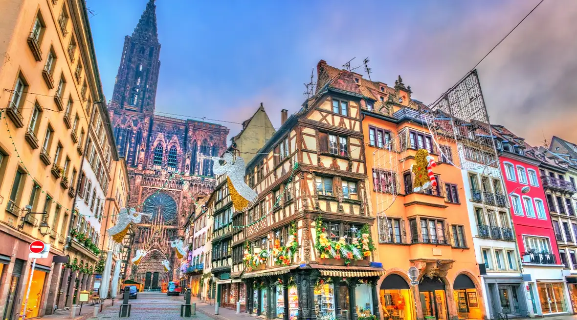 Colourful old buildings on cobbled street covered in Christmas lights with cathedral in background