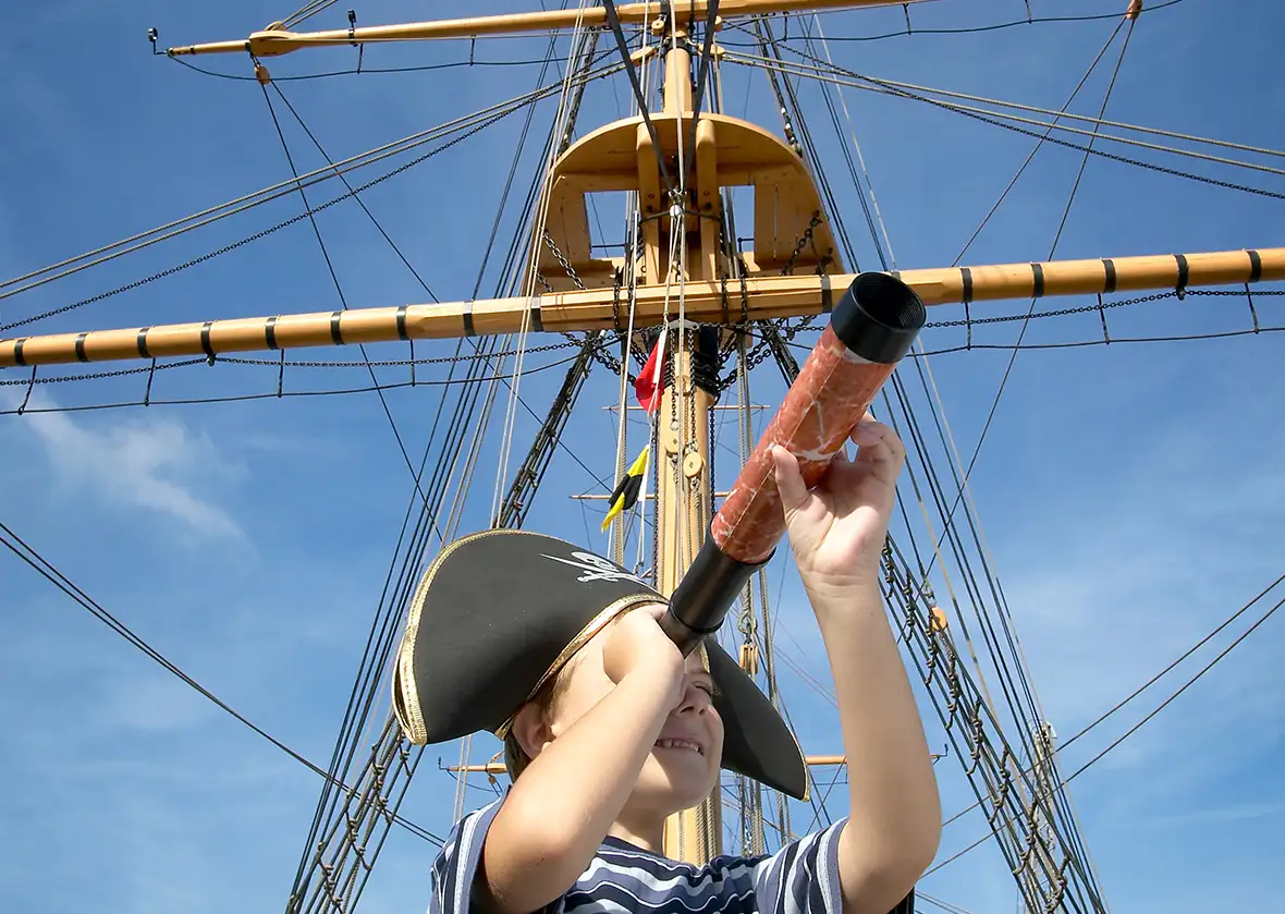 kind met piratenmuts en verrekijker op historisch zeilschip