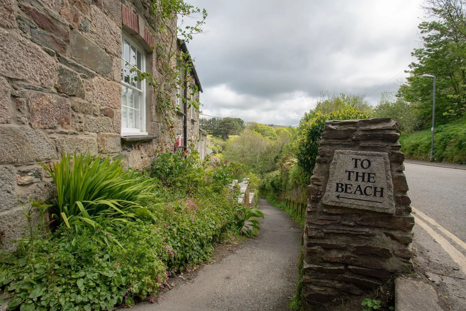 Wegweiser mit der Aufschrift ‘Zum Strand’ neben einem Fußweg und alten Cottages.