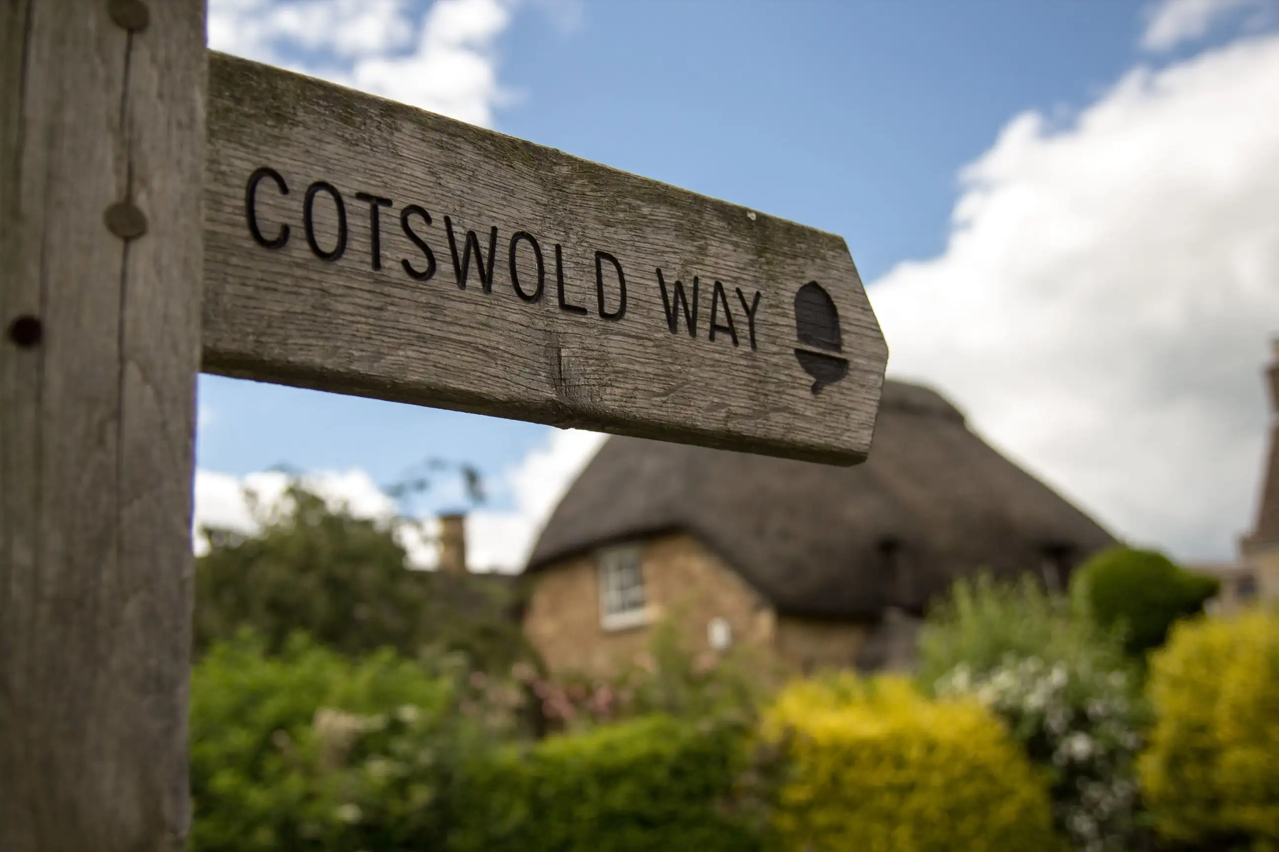 Wegwijzer van de Cotswold Way bij een huisje met een rieten dak.
