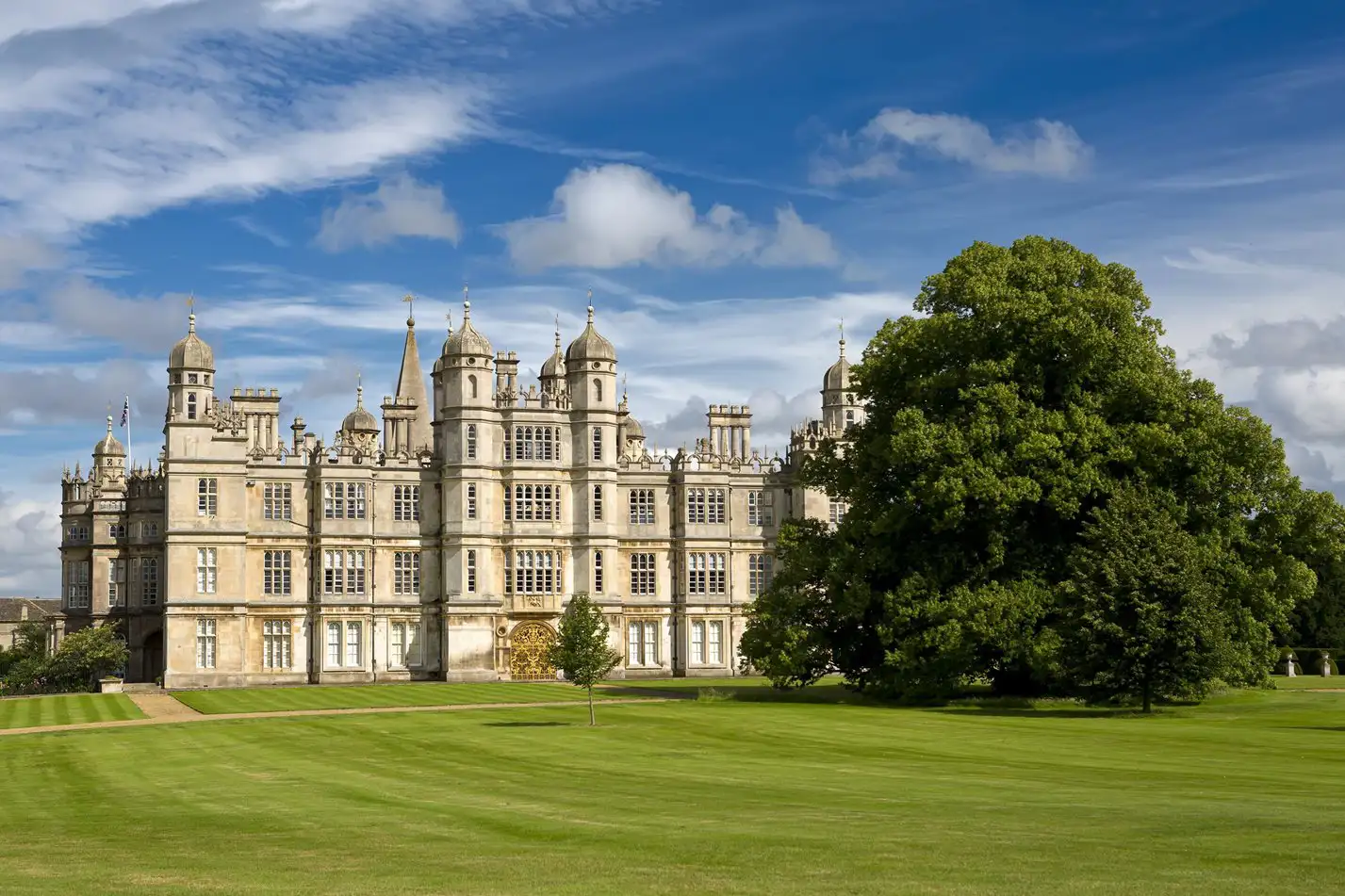 Burghley House aan een grasveld met een enorme boom.