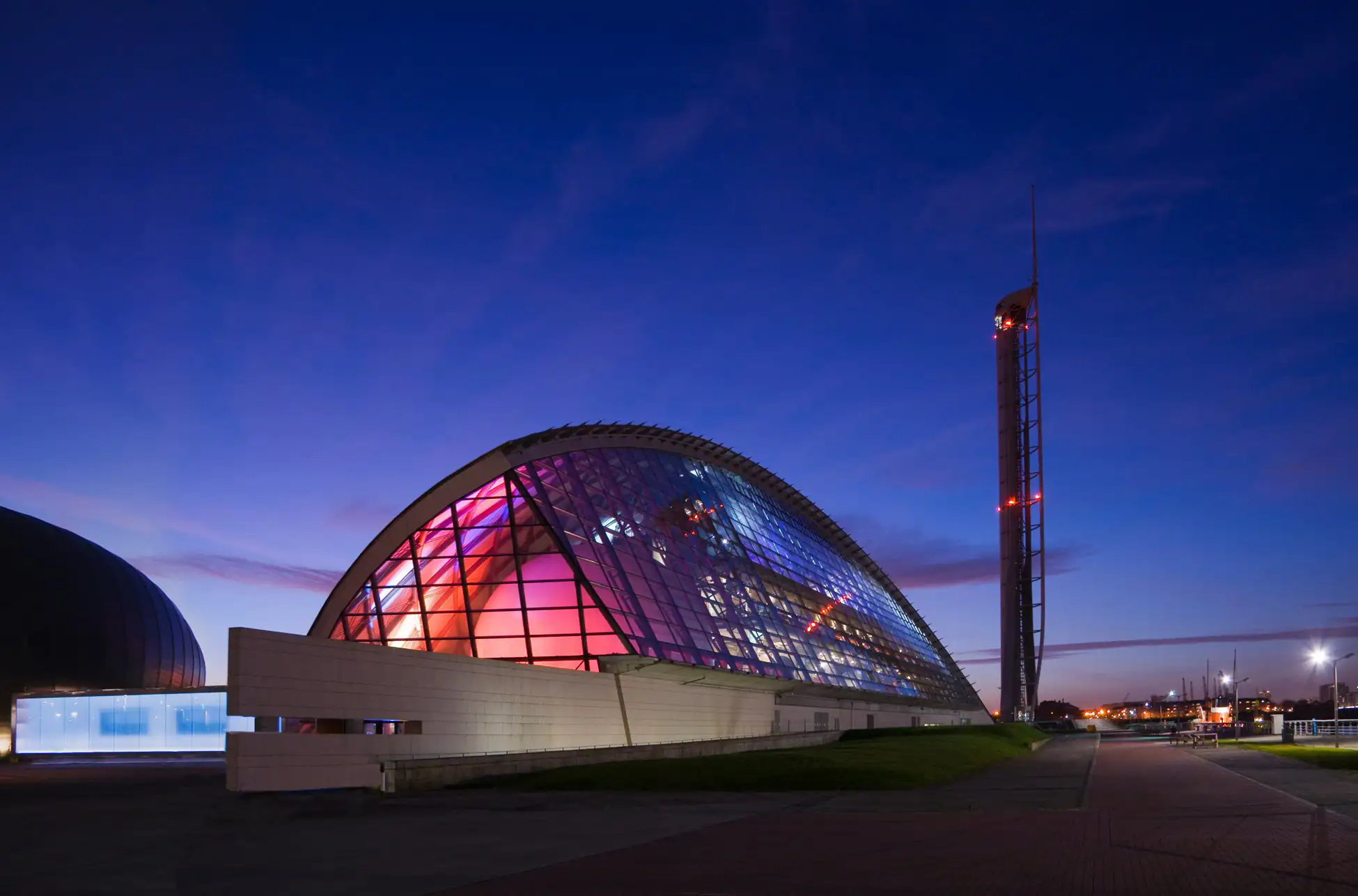 Een modern wigvormig glazen gebouw bij zonsondergang
