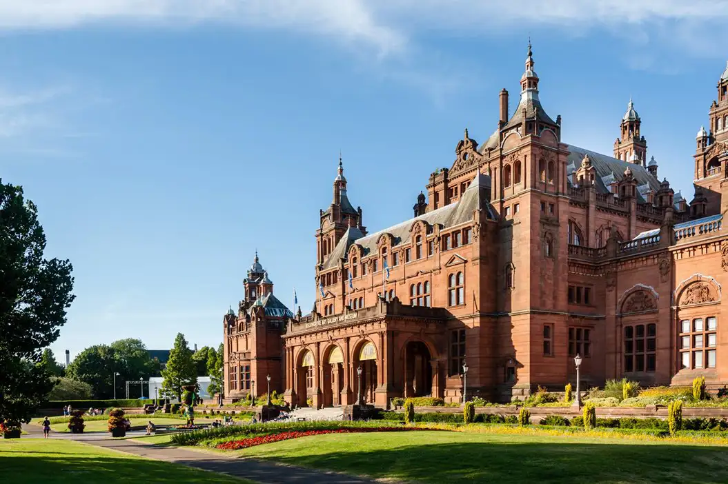 Een groot terracotta neogotisch gebouw met mooie tuinen
