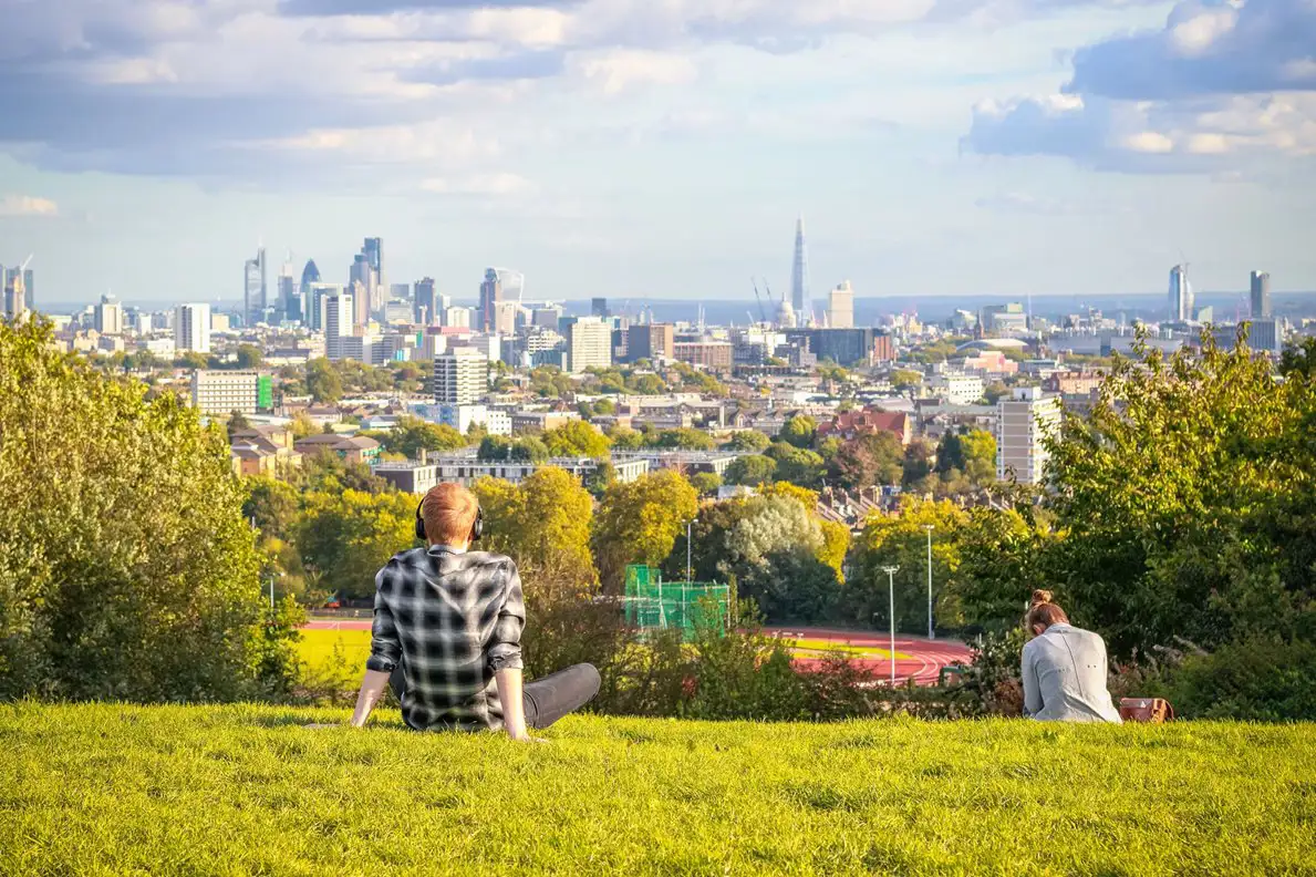 Twee mensen zitten op een grasveld en kijken uit op de stad Londen.