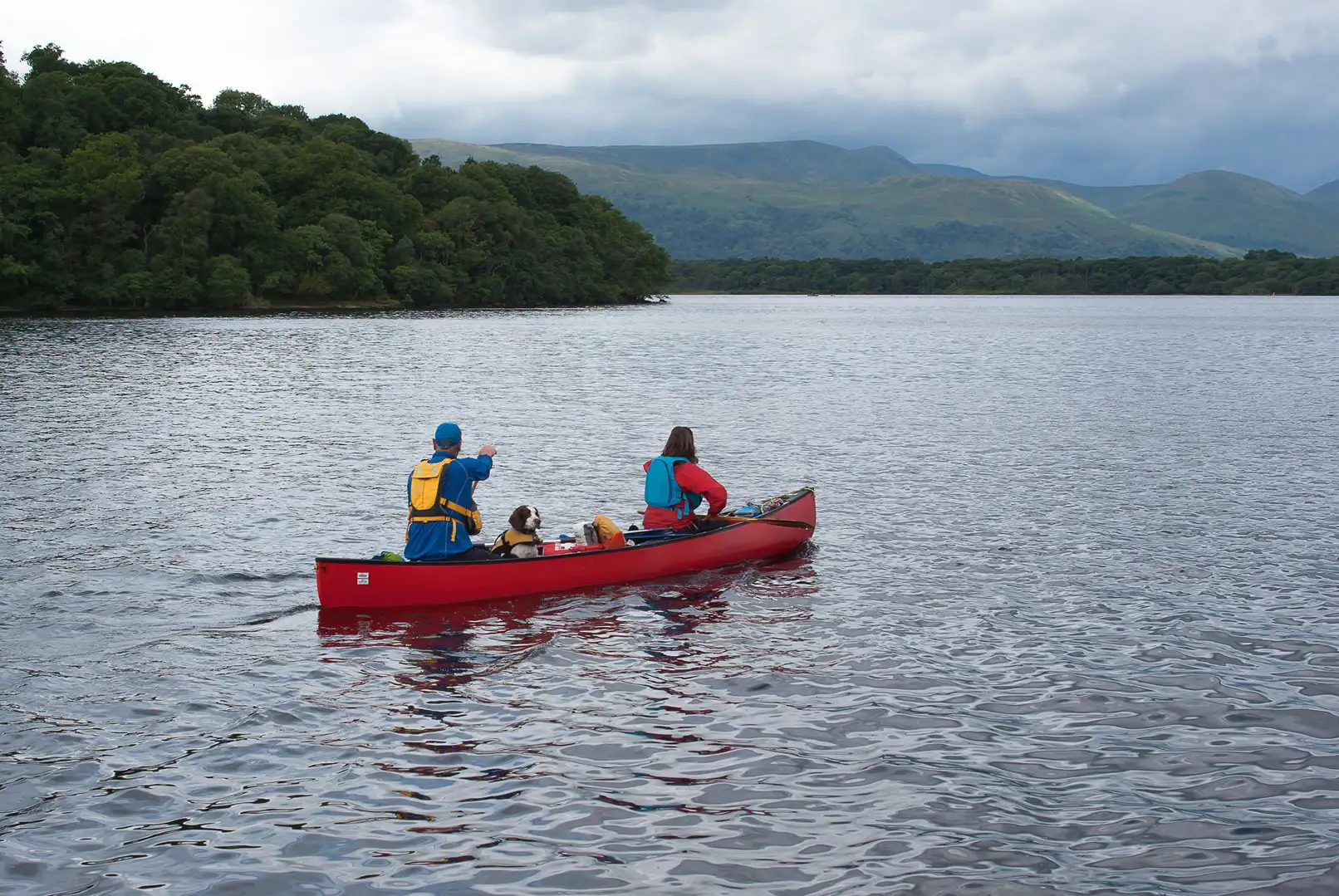 Twee personen en een hond kanoën op Loch Lomond, Schotland.
