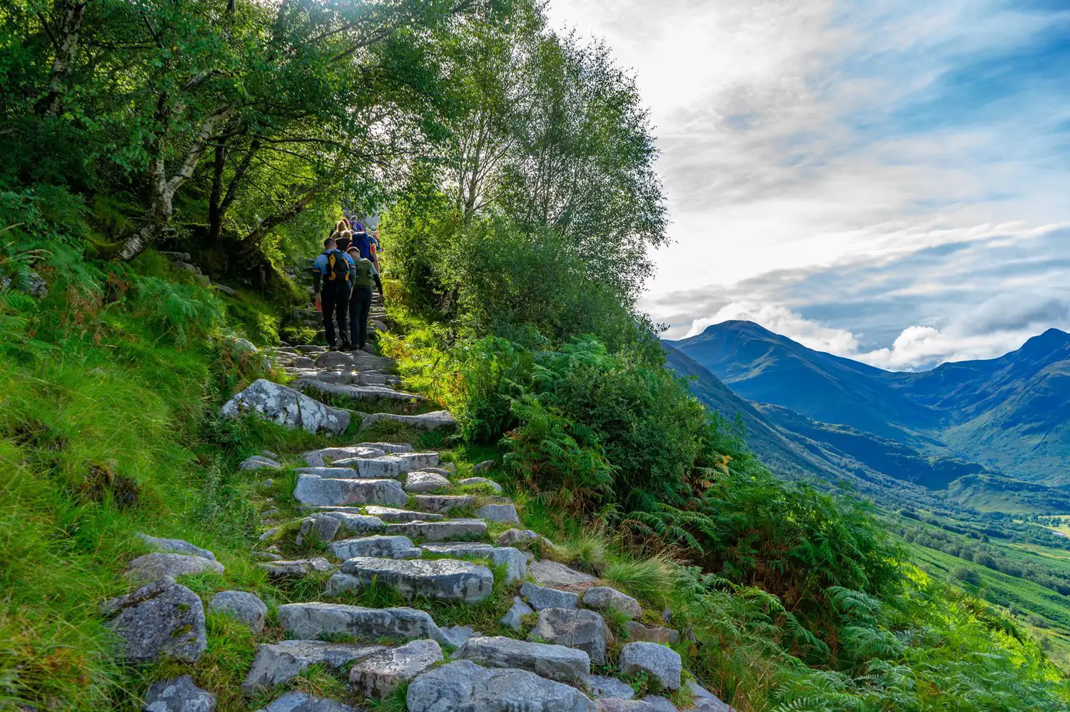 Wandelaars lopen op een steil rotsachtig pad met bergen in de verte.