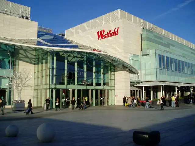 La façade de Westfield Shopping sous un ciel bleu avec des personnes qui entrent et qui sortent.
