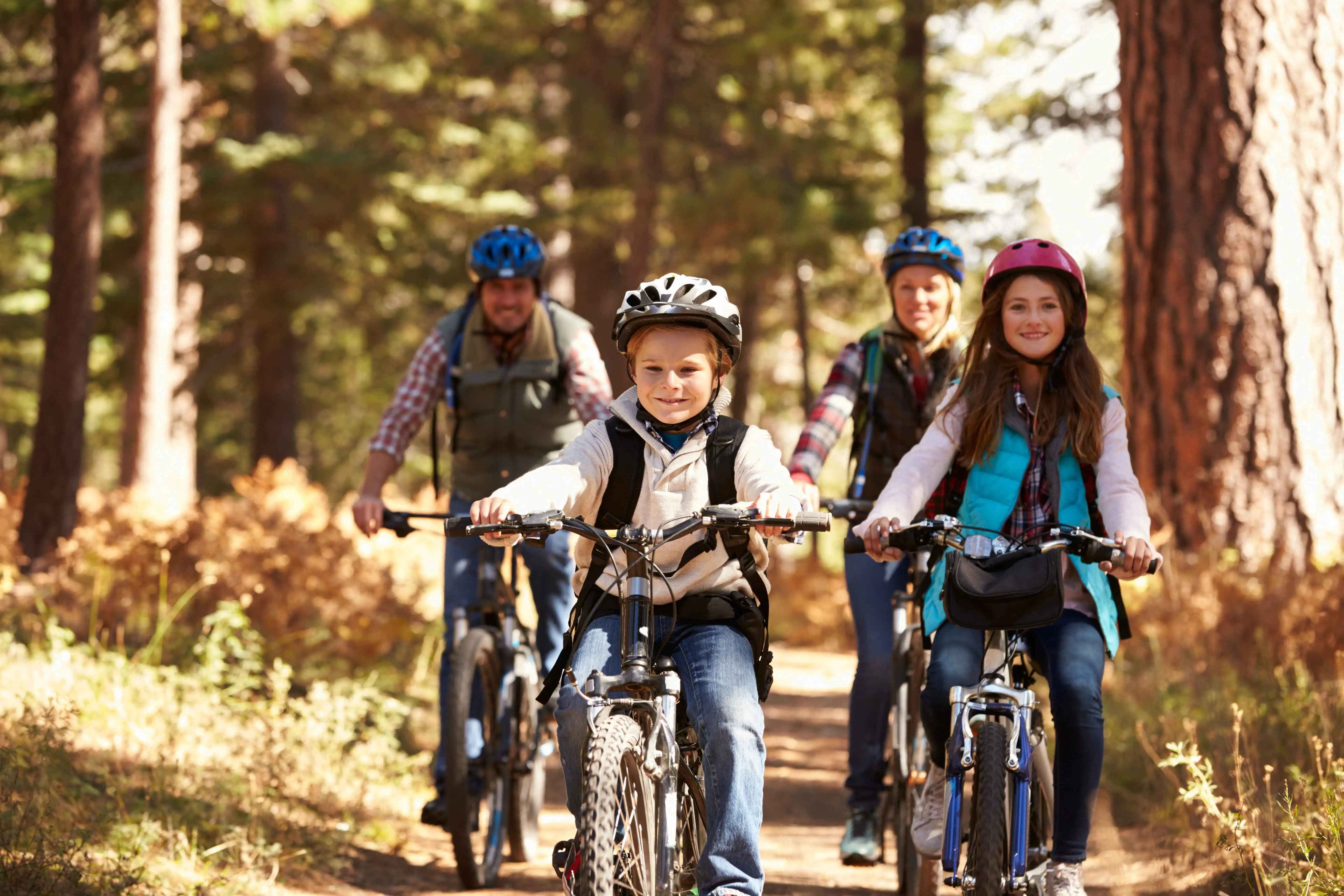 A family cycling towards the camera on a scenic path lined with vibrant autumn foliage.