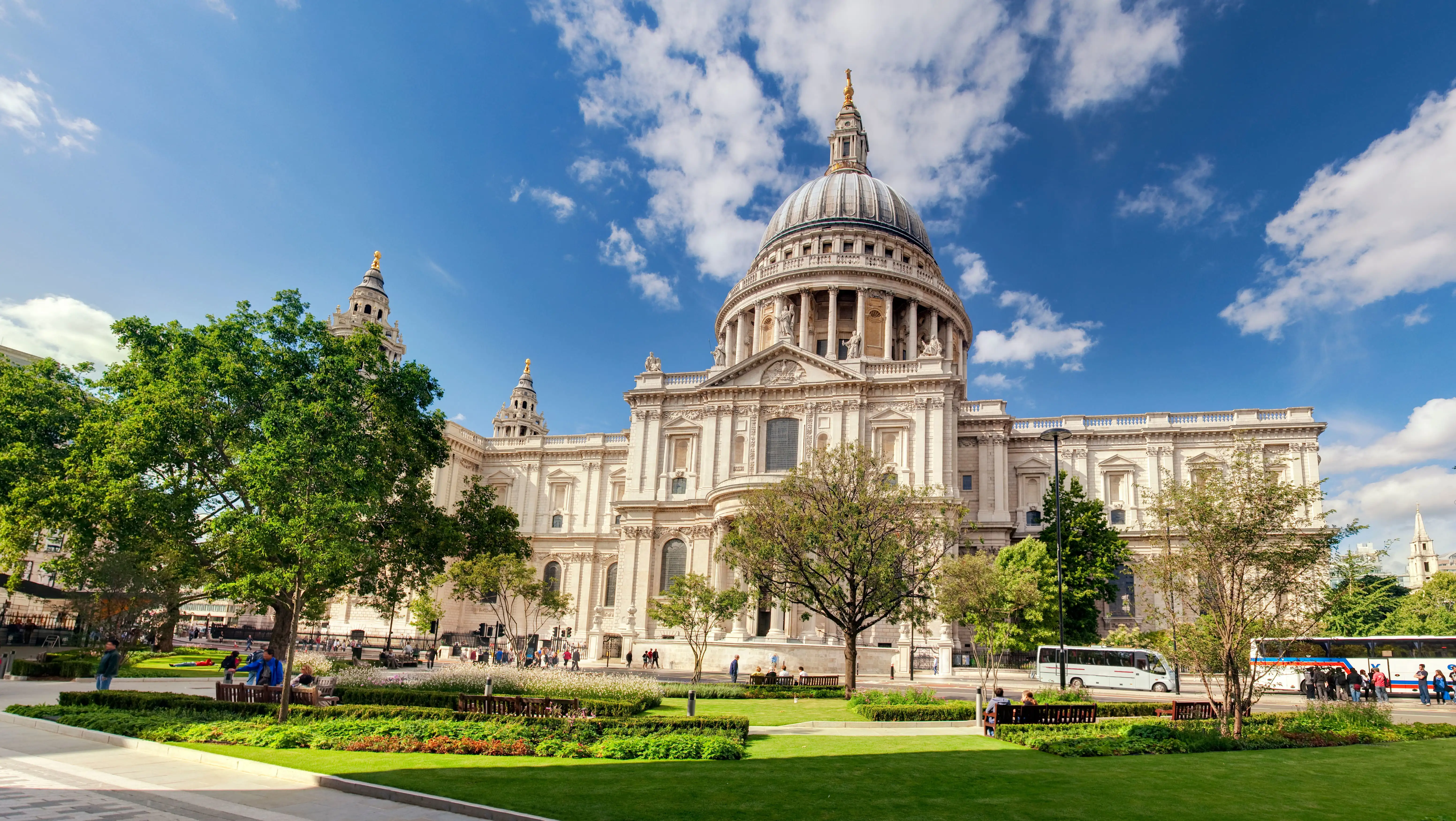 La cathédrale St. Paul à Londres, avec son célèbre dôme, entourée de verdure sous un ciel bleu.