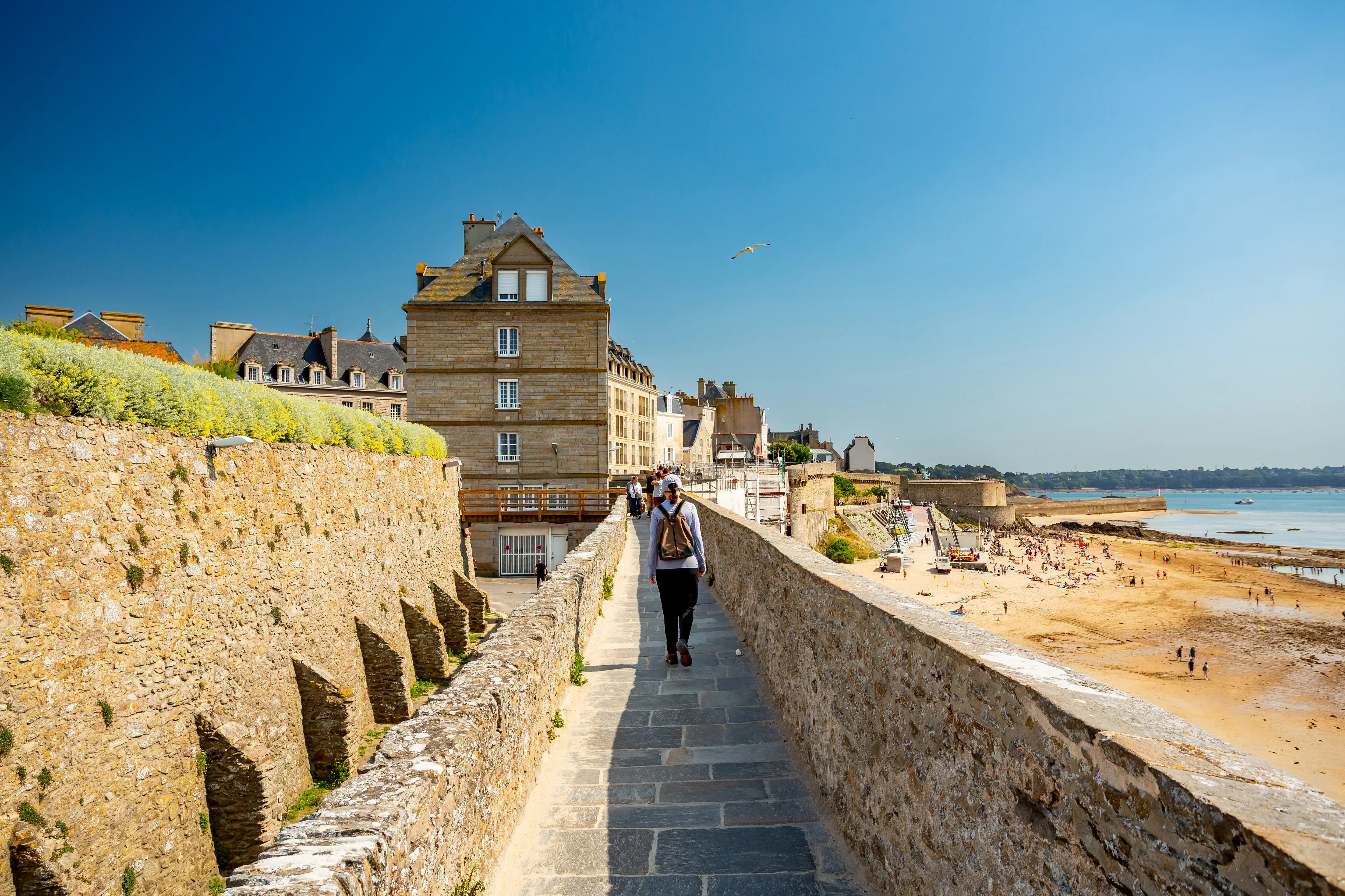 Person walking along a sea wall overlooking a beach