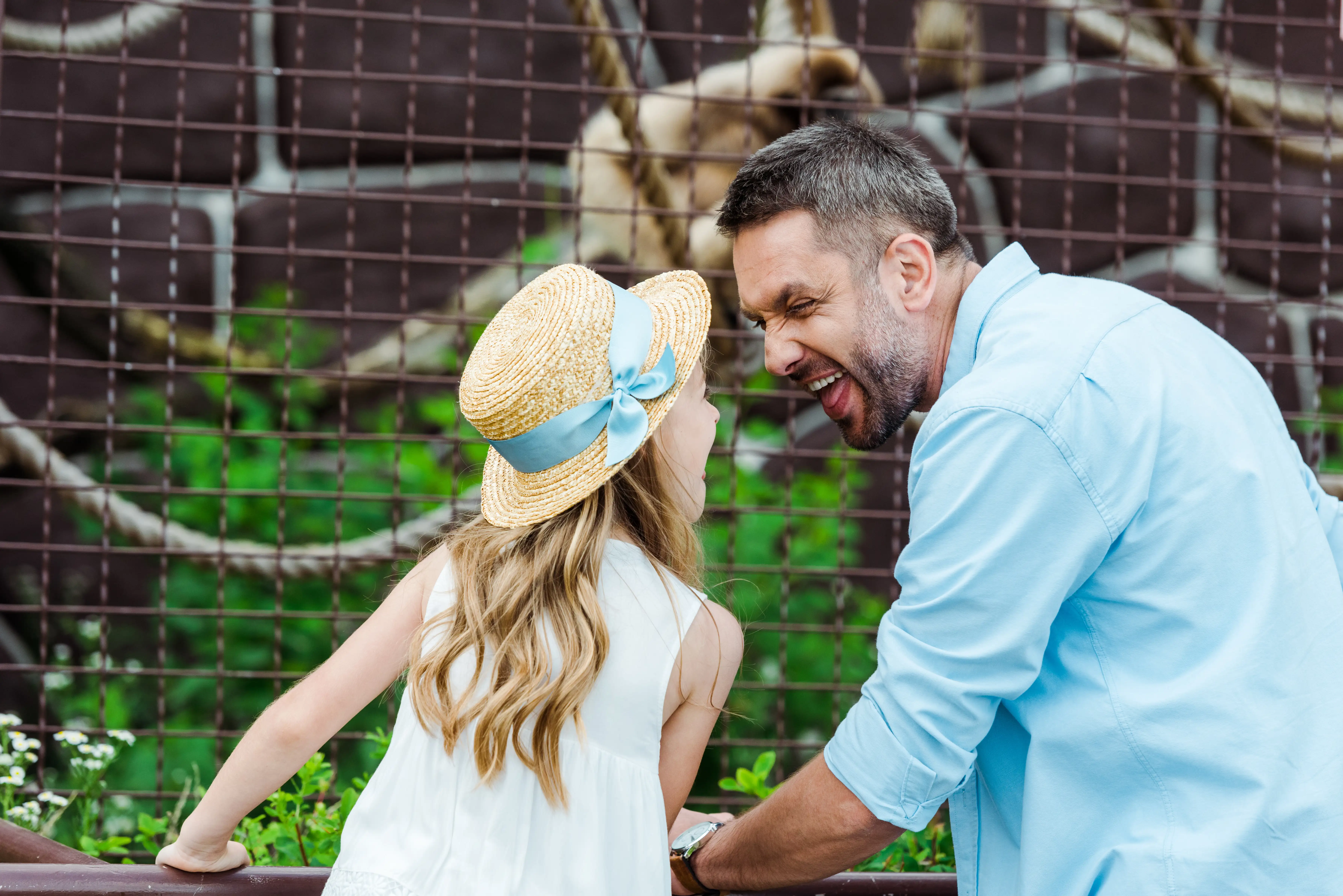 Father and daughter pulling smile faces at the zoo.