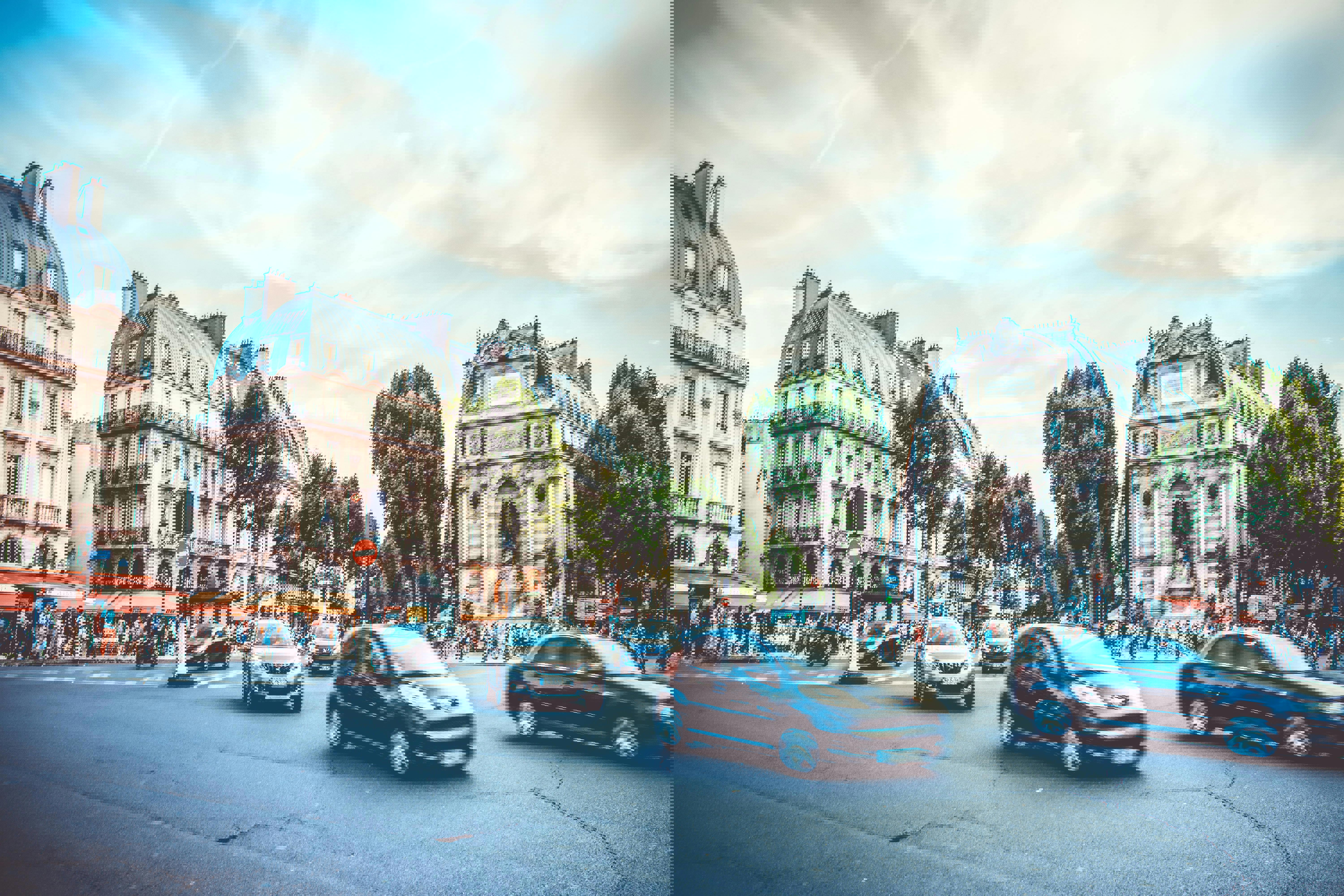 Cars driving through an intersection in Paris. Busy streets and the Fontaine Saint-Michel fountain is in the background.