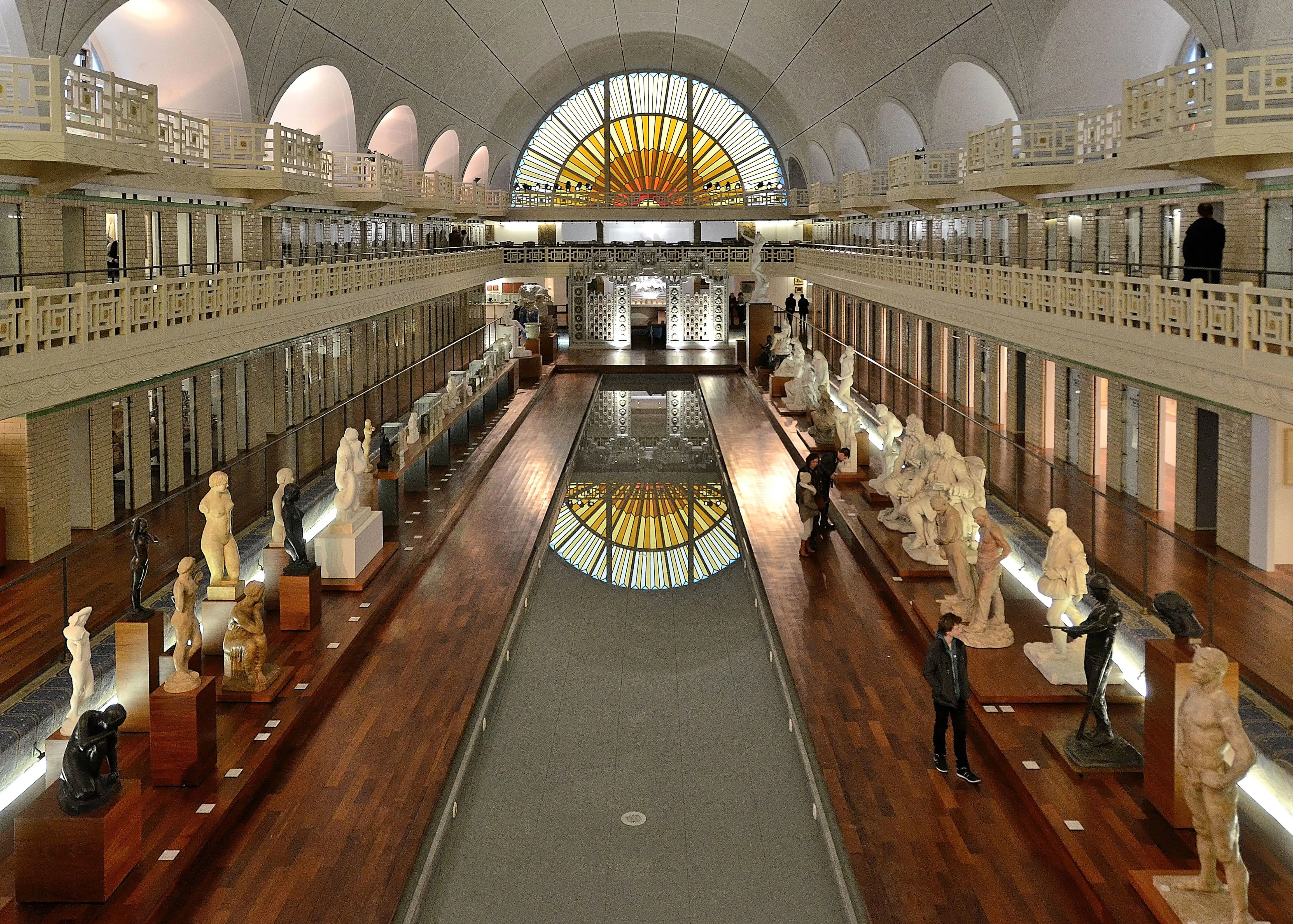People looking at sculptures in an exhibition hall with a long pool of water in the middle, La Piscine, Roubaix