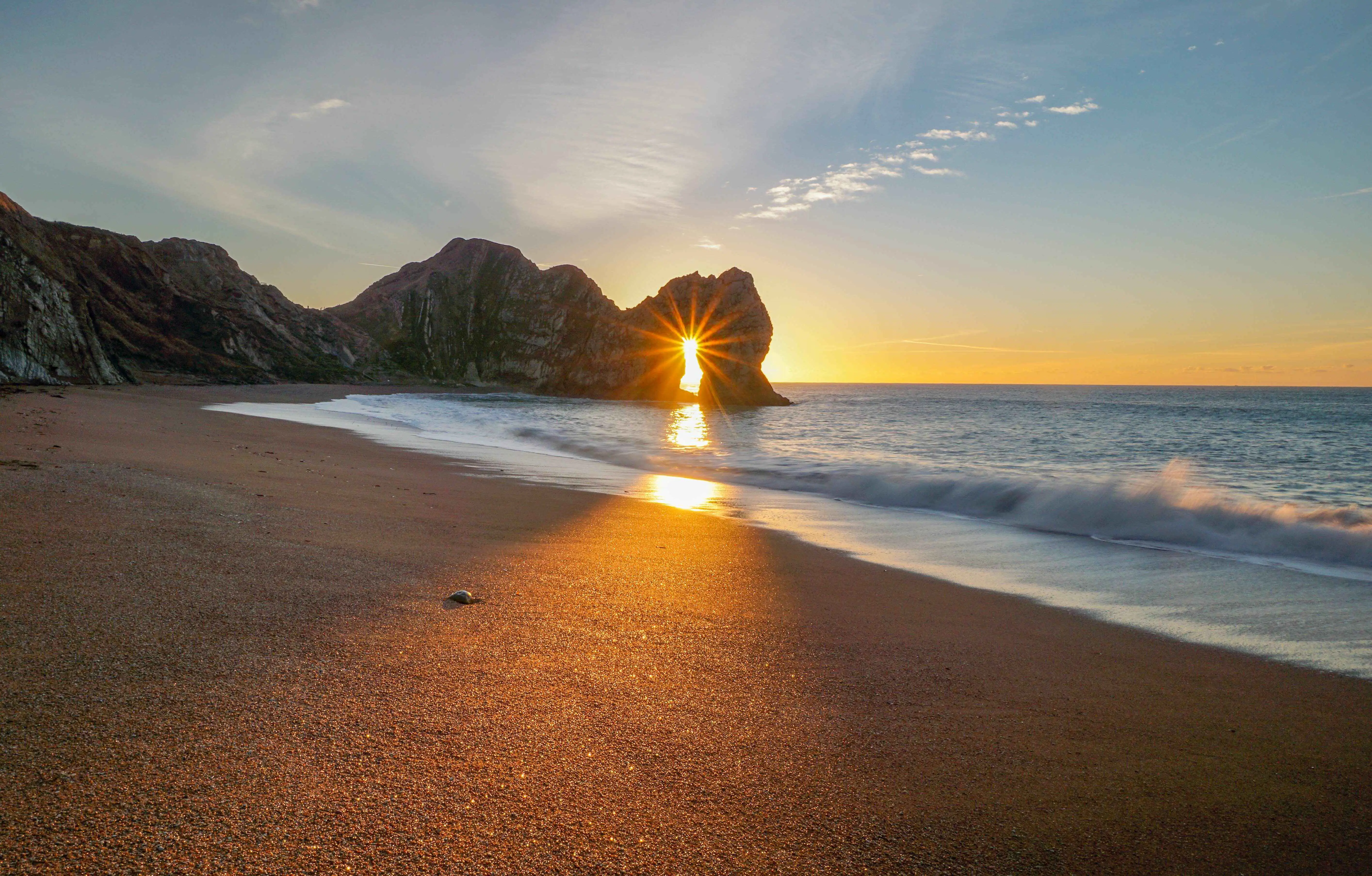 Durdle Door avec le soleil parfaitement encadré dans son arche de calcaire, créant un effet époustouflant.