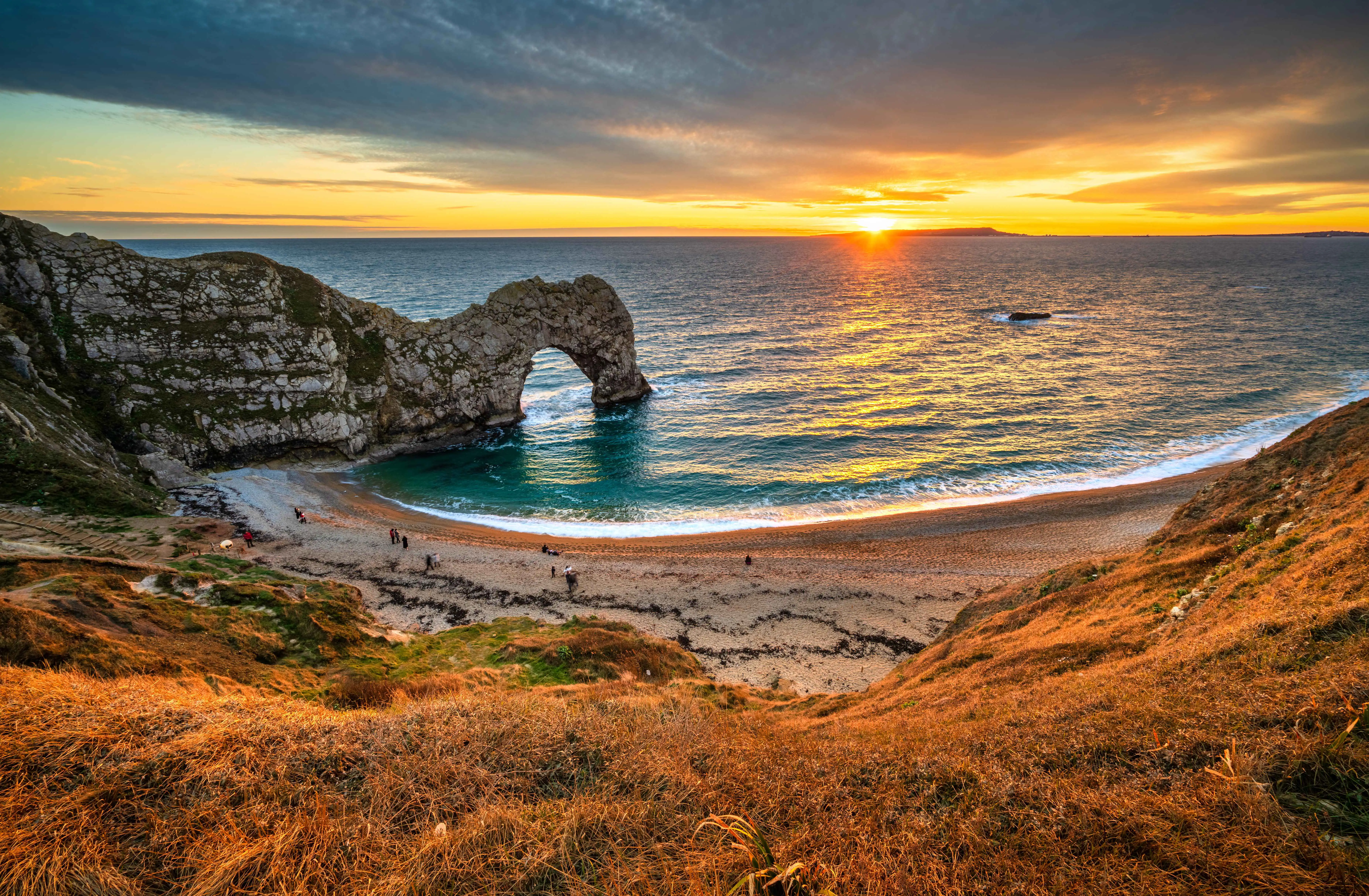Durdle Door au coucher de soleil avec une lumière dorée qui baigne la plage.